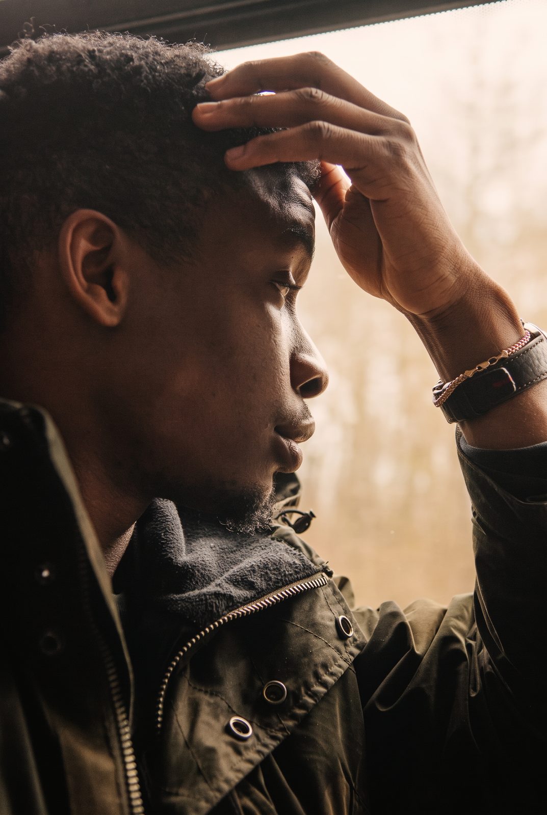 Young man sitting by a bright window, resting a hand on his forehead as he takes a quiet breath, anxiety and overthinking therapy online across Ontario
