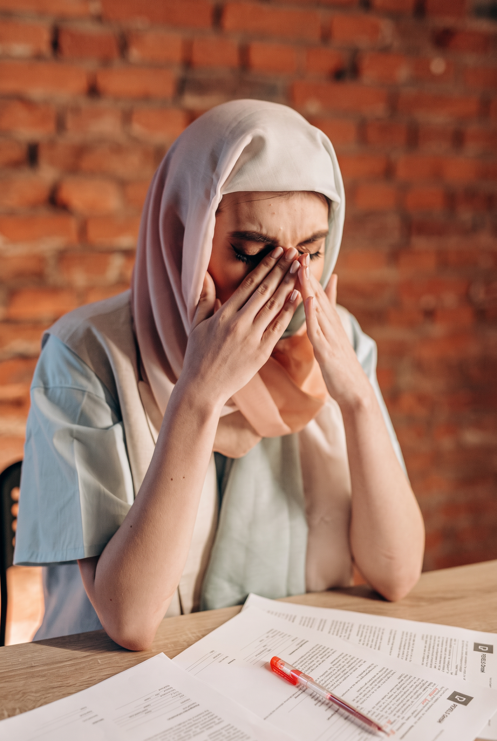 Woman in a hijab at her desk with her head in her hands, therapy for professional and caregiver burnout with an online therapist in Ontario