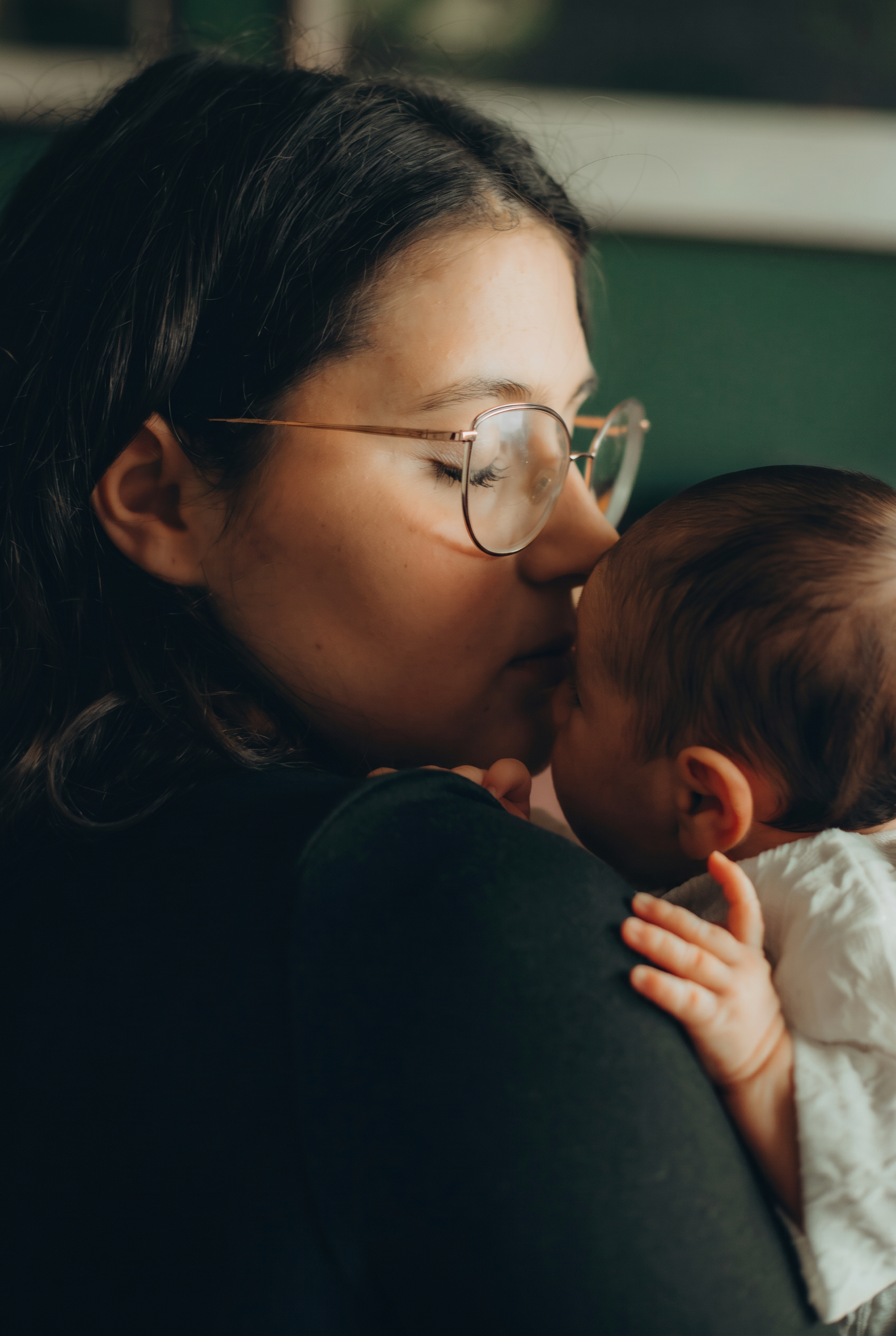 South Asian mother in glasses gently kissing her baby, postpartum adjustment and new parent therapy with Tanika Newman, RSW, serving Ontario virtually